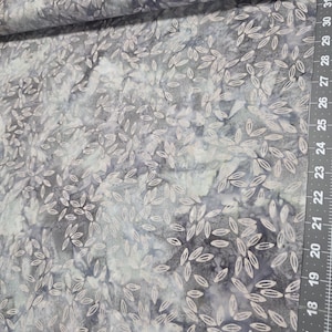 May include: Fabric with a gray and blue watercolor-style background. The fabric is patterned with small, white leaf-like shapes. A ruler with inch measurements is visible along the right edge of the fabric.