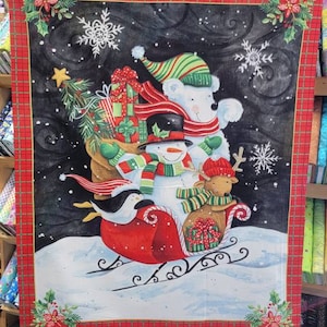 May include: A Christmas-themed fabric panel featuring a polar bear, snowman, and reindeer riding a red sleigh through a snowy landscape. The panel has a red plaid border with holly and snowflake accents. Presents and a penguin are also visible.