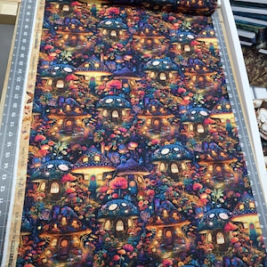 May include: A vibrant fabric roll featuring a whimsical mushroom village design. The pattern showcases colorful mushroom houses with glowing windows, surrounded by flowers and foliage in shades of blue, purple, orange, and pink. The fabric is on a wooden surface with a ruler.