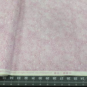 May include: Pink fabric with a pattern of small, white, and light pink circles. The fabric is folded, showing the pattern across the surface. The text "Essentials Copyright Wilmington Prints. All Rights Reserved." is visible.