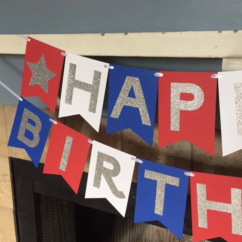 Puede incluir: Bandera roja, blanca y azul con letras de purpurina plateada que deletrean "Happy Birthday".