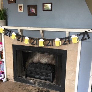 Pu&ograve; includere: Uno striscione di compleanno nero e giallo per il 21&deg; compleanno con boccali di birra appesi. Lo striscione &egrave; appeso sopra un camino.
