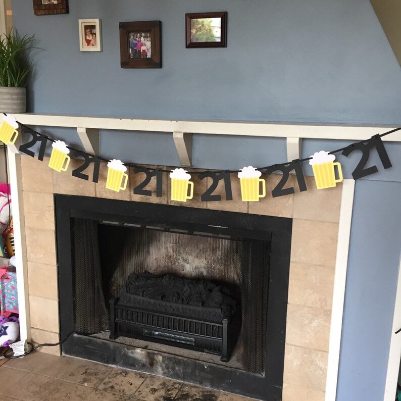 Pu&ograve; includere: Uno striscione di compleanno nero e giallo per il 21&deg; compleanno con boccali di birra appesi. Lo striscione &egrave; appeso sopra un camino.