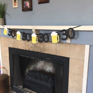 May include: Black and yellow paper banner with the number 30 and beer mugs, hanging above a fireplace.