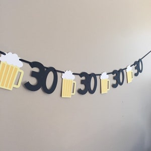 May include: Black and yellow paper banner with the number 30 repeated and beer mug cutouts. The banner is strung together with black string.