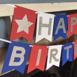 Puede incluir: Bandera roja, blanca y azul con letras de purpurina plateada que deletrean "Happy Birthday".