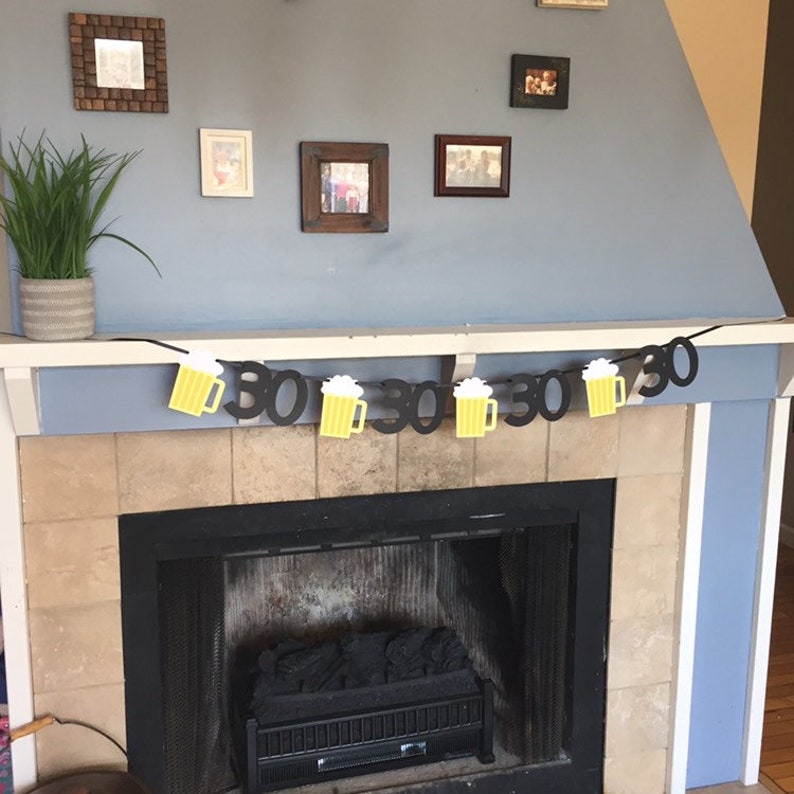 May include: A black and yellow banner with beer mugs and the number 30 repeated. The banner is hanging above a fireplace.