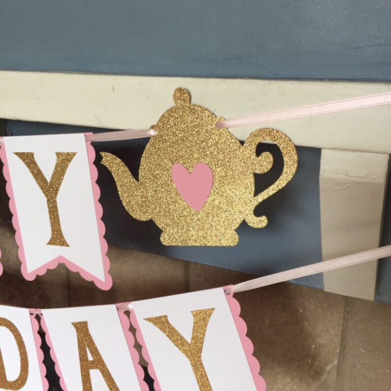 May include: Gold glitter "Happy Birthday" banner with pink scalloped edges and a gold glitter teapot with a pink heart.