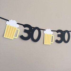 May include: Black and yellow paper banner with the number 30 and beer mug cutouts. The banner is strung together with black string.