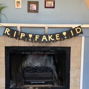 May include: Black and gold banner with the text "RIP FAKE ID" with gold wine glass icons between the words.