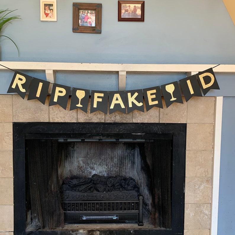 May include: Black and gold banner with the text "RIP FAKE ID" with gold wine glass icons between the words.