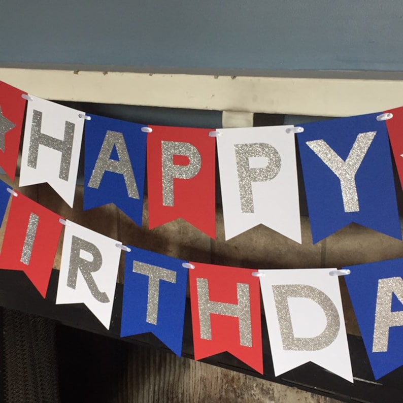 Puede incluir: Bandera roja, blanca y azul con letras de purpurina plateada que deletrean "Happy Birthday".