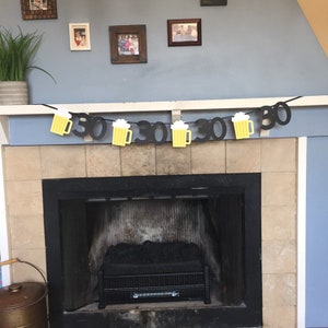 May include: A black and yellow banner with beer mugs and the number 30 repeated. The banner is hanging above a fireplace.
