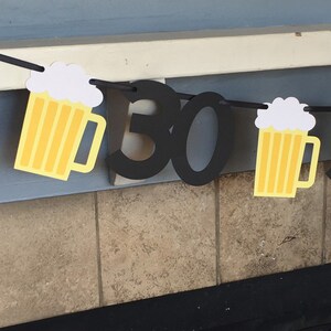 May include: A black and yellow birthday banner with the number 30 and beer mug designs. The banner is hanging on a wall.