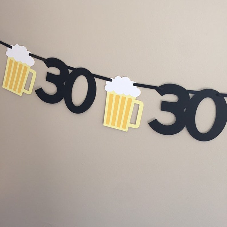 May include: Black and yellow paper banner with the number 30 and beer mug cutouts. The banner is strung together with string.