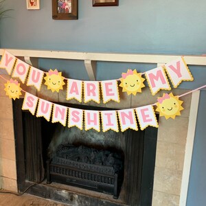 May include: A yellow and pink banner with the text "You are my sunshine" and sun illustrations. The banner is hanging above a fireplace.