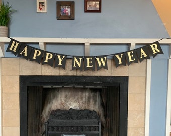 May include: A black banner with gold lettering that reads "HAPPY NEW YEAR" hangs above a fireplace. The fireplace has a black interior and a decorative grate. The wall is painted blue and has framed pictures.