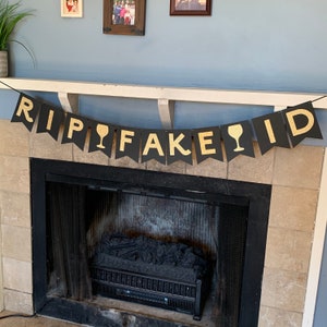 May include: Black and gold banner with the text "RIP FAKE ID" and wine glass icons. The banner is hanging above a fireplace.