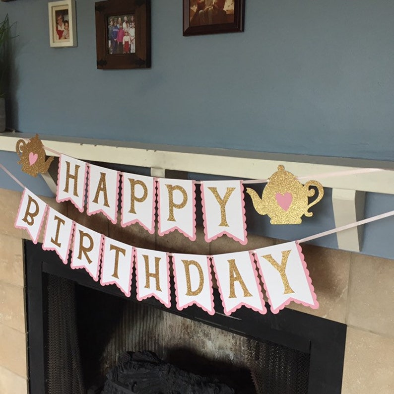 May include: A pink and white banner with gold glitter letters that reads "Happy Birthday". The banner is decorated with two gold glitter teapots with pink hearts.