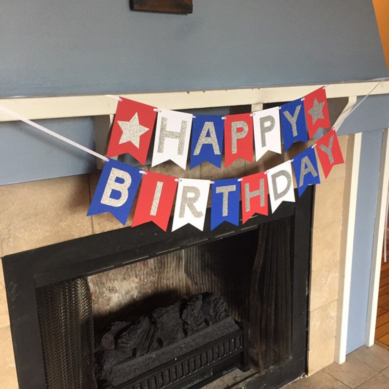 Puede incluir: Una pancarta roja, blanca y azul con letras plateadas brillantes que dice "Happy Birthday". La pancarta est&aacute; colgada sobre una chimenea.