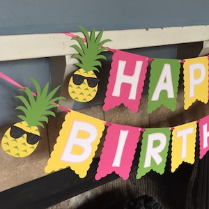 May include: A colorful Happy Birthday banner with green, yellow, and pink scalloped flags. Each flag has a white letter, and there are two pineapple cutouts with sunglasses.
