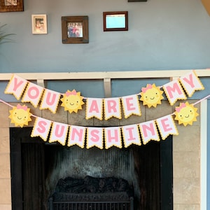 May include: A yellow and pink banner with the text "You are my sunshine" and smiling sun faces. The banner is hanging above a fireplace.