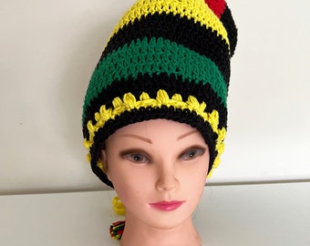 Op de afbeelding: Een gebreide beanie met strepen in geel, groen en zwart. De muts heeft een rode pompon bovenop en een gele, groene en rode kwast die eronder hangt.