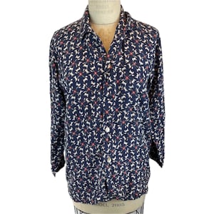 Könnte beinhalten: Marineblaues Button-Down-Hemd mit einem sich wiederholenden Muster aus weißen Hundesilhouetten und roten Akzenten. Das langärmlige Hemd hat einen klassischen Kragen und wird auf einer Schaufensterpuppe präsentiert. Das Hemd ist aus weichem, leichtem Stoff.