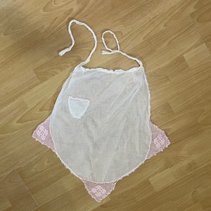 May include: A white apron with a pink crocheted trim and a small pocket.