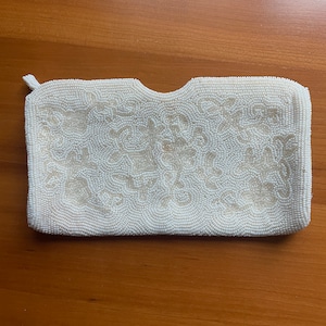 May include: A white beaded clutch purse with a floral design. The purse has a small flap closure and a beaded strap.