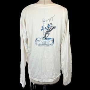 May include: Cream-colored long-sleeve shirt featuring a cartoon graphic on the back. The graphic depicts a bear-like character skiing, with the words "Big A Snowbird" in blue. The shirt has a crew neck and raglan sleeves.