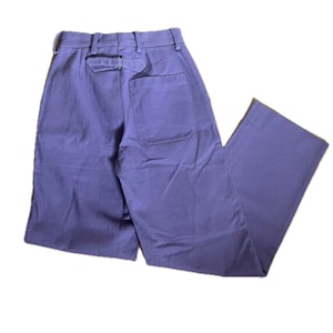May include: Lavender trousers featuring a high-waisted design with belt loops, a rear cinch strap with a metal buckle, and a single patch pocket on the back. The fabric has a smooth texture, and the word GOLF is embossed on the back pocket.