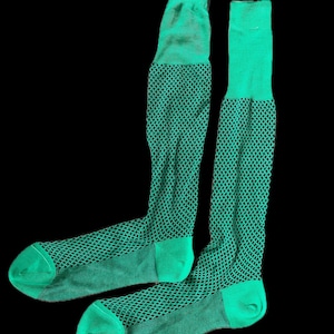 May include: A pair of knee-high socks in a vibrant green color. The socks feature a textured, diamond-patterned design on the leg and foot, with solid green cuffs and toes. The background is solid black.