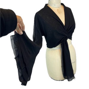 May include: A black long-sleeve top featuring a deep V-neckline and a front-tie knot detail. The garment is made of a sheer, lightweight fabric and includes dramatic, wide bell sleeves that flare out from the elbow to the wrist.