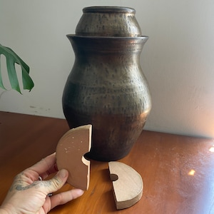 May include: A brown ceramic jar with a lid and two brown ceramic circles with a hole in the center.