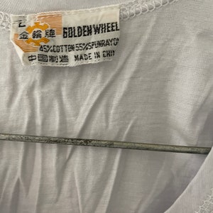 May include: A white t-shirt with a yellow tag that reads "Golden Wheel 45% Cotton 55% Spunrayon Made in China" in English and Chinese.
