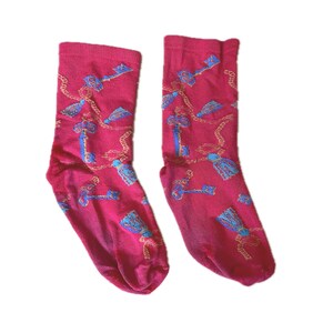 May include: A pair of magenta crew socks featuring a repeating pattern of blue keys and gold chains. The design includes small blue tassels interspersed among the keys and chains, creating a detailed graphic print across the fabric of the socks.