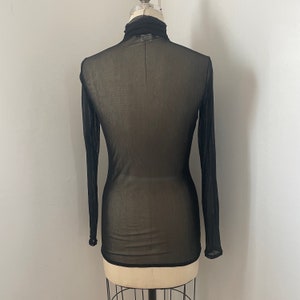 May include: Black sheer long-sleeved turtleneck top on a mannequin.