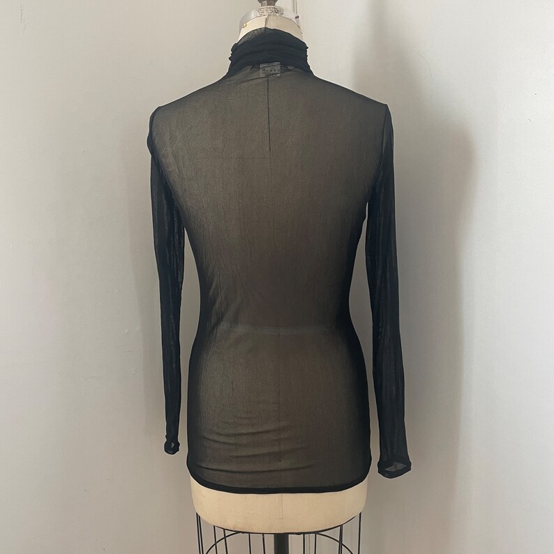 May include: Black sheer long-sleeved turtleneck top on a mannequin.