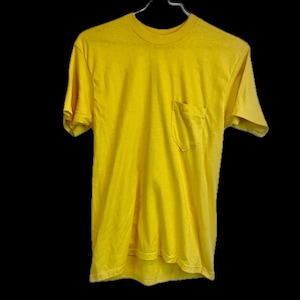 May include: A bright yellow t-shirt with a chest pocket, hanging on a metal hanger against a black background. The short-sleeved shirt has a crew neck and a slightly worn appearance, suggesting it's been washed.