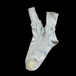 Può includere: Un paio di calze grigio chiaro con polsini a coste. Le calze presentano una scritta stampata in blu che recita "FEELS SOFTER - stronger with - nylon - Randolph Knit" e una piccola etichetta rettangolare nella zona della punta.