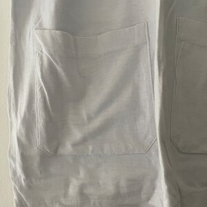 May include: A white garment with two large pockets on the front. The pockets have a simple design and are sewn with a straight stitch.
