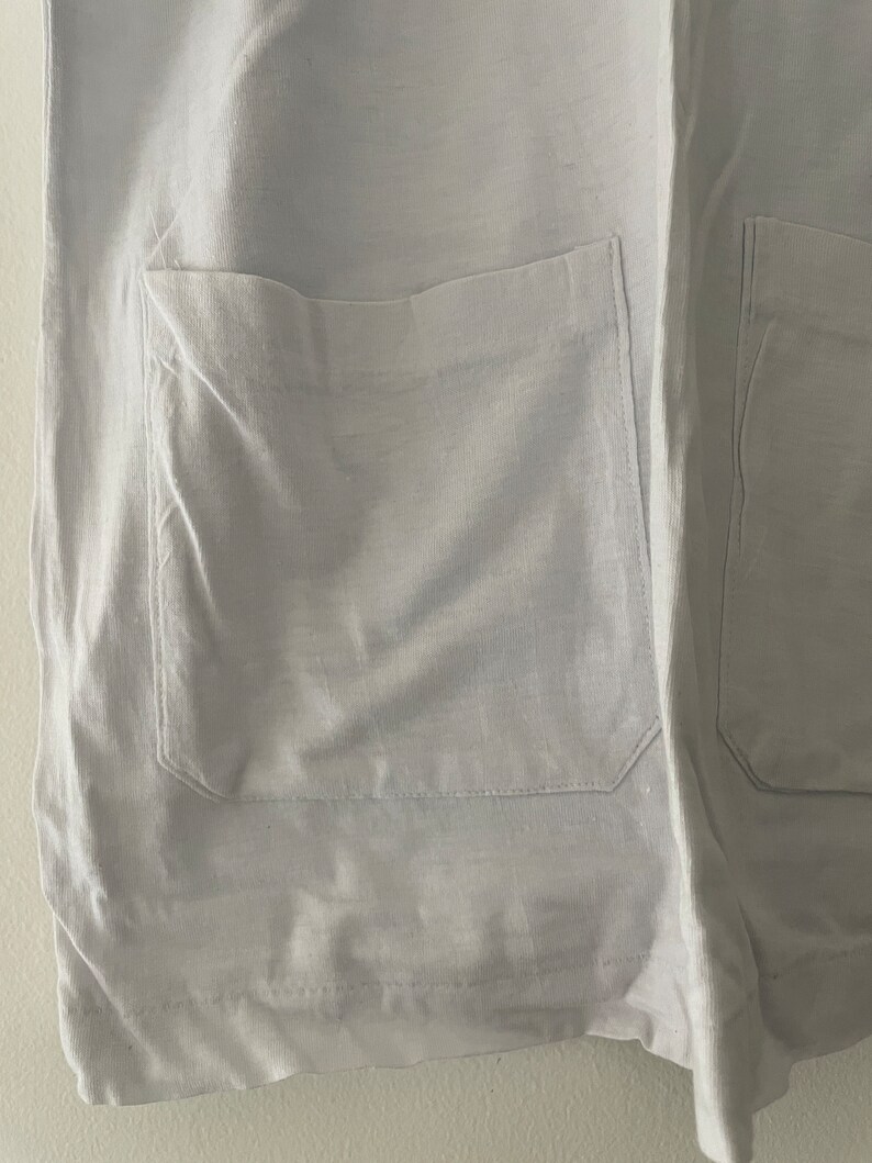 May include: A white garment with two large pockets on the front. The pockets have a simple design and are sewn with a straight stitch.
