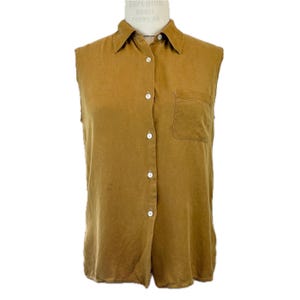 May include: Mustard-colored sleeveless button-down shirt with a collared neckline and a single chest pocket. The shirt is displayed on a mannequin and features white buttons down the front.