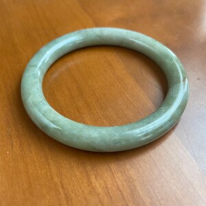 May include: A light green jade bangle bracelet. The bangle is smooth and polished.