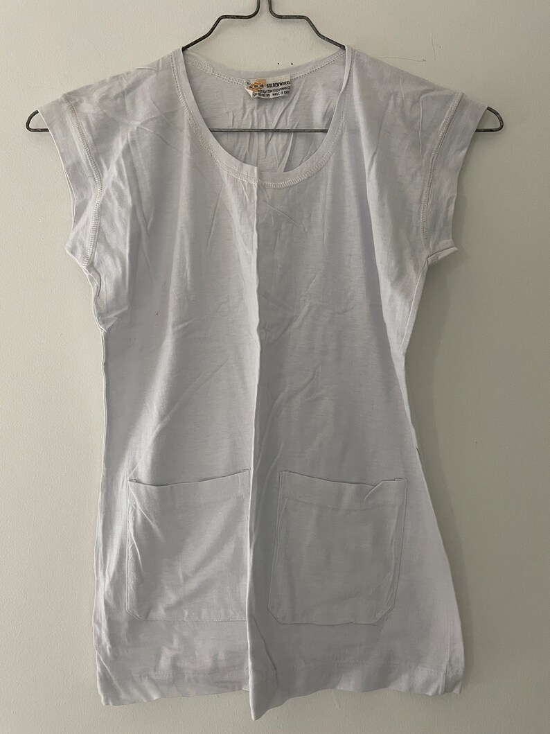 May include: A light gray t-shirt with short sleeves and two patch pockets. The shirt has a round neckline and is hanging on a hanger.