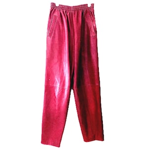 以下が含まれることがあります： 赤い革のパンツ。ウエストはゴム入りで、両サイドにポケットが2つ付いています。ストレートレッグカットで、滑らかで光沢のある革素材で作られています。色は深みのある鮮やかな赤色です。
