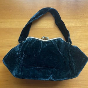 May include: A black velvet evening bag with a silver clasp. The bag has a rounded shape and a short handle.