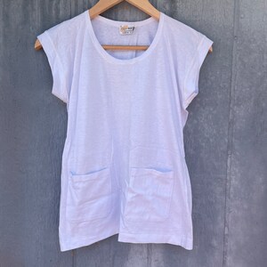 May include: White cotton t-shirt with short sleeves and two patch pockets. The shirt has a round neckline and a relaxed fit.