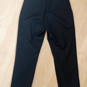 May include: Black dress pants with a high waist and a straight leg. The pants have two back pockets and a button and zipper closure. The fabric appears to be a smooth, woven material.